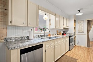 Une cuisine avec des meubles de couleur claire, un plan de travail en granit, un lave-vaisselle, une cuisinière et une fenêtre donnant sur l’extérieur.