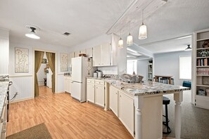 Una cocina amplia con piso de madera, muebles blancos y lámparas colgantes.
