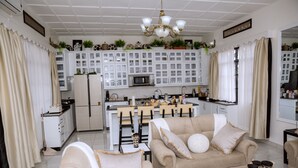 A spacious living room with a beige sofa and a dining area with a kitchen in the background.