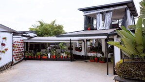A modern building with a covered patio area featuring potted plants and a staircase leading to an upper level.