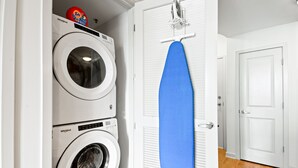 Zona de lavandería con dos lavadoras Whirlpool y una tabla de planchar azul apoyada en una puerta blanca.