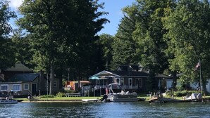 A lakeside property with a dock, a boat, and a house with a covered patio. - Keeney Kottage (Six Lakes)