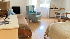 Un dormitorio con una cama, un escritorio, una silla, un ventanal con persianas, un televisor y un cartel en la pared.