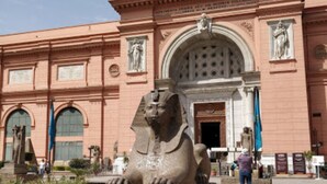 A large stone sphinx statue in front of a pink building with arched windows and columns. - City inn hotel  (Cairo)