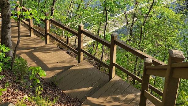 A wooden boardwalk with railings, surrounded by lush green trees and a body of water in the background. - Beautiful waterfront lodge, private dock and breath taking views of Smith Mt. (Pittsville)