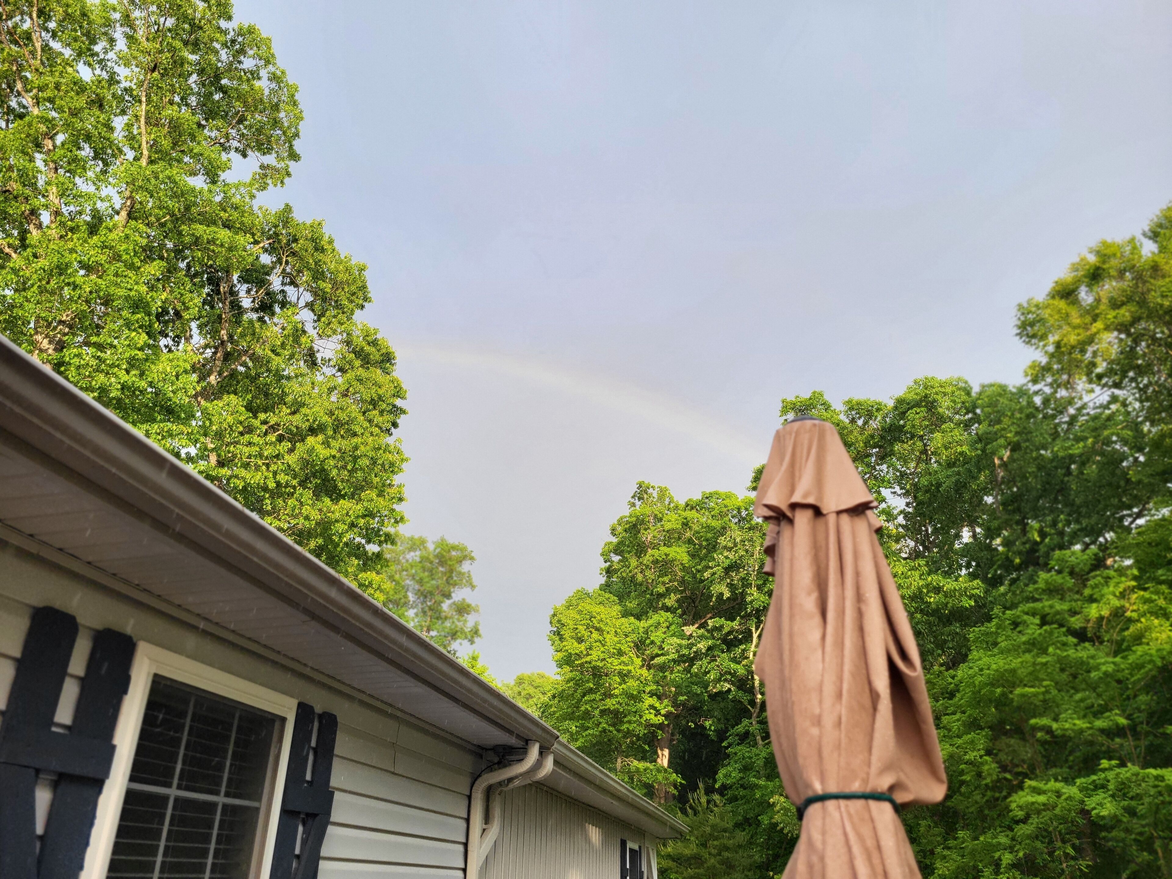 Une maison dotée d’un patio couvert, entourée d’arbres verdoyants.