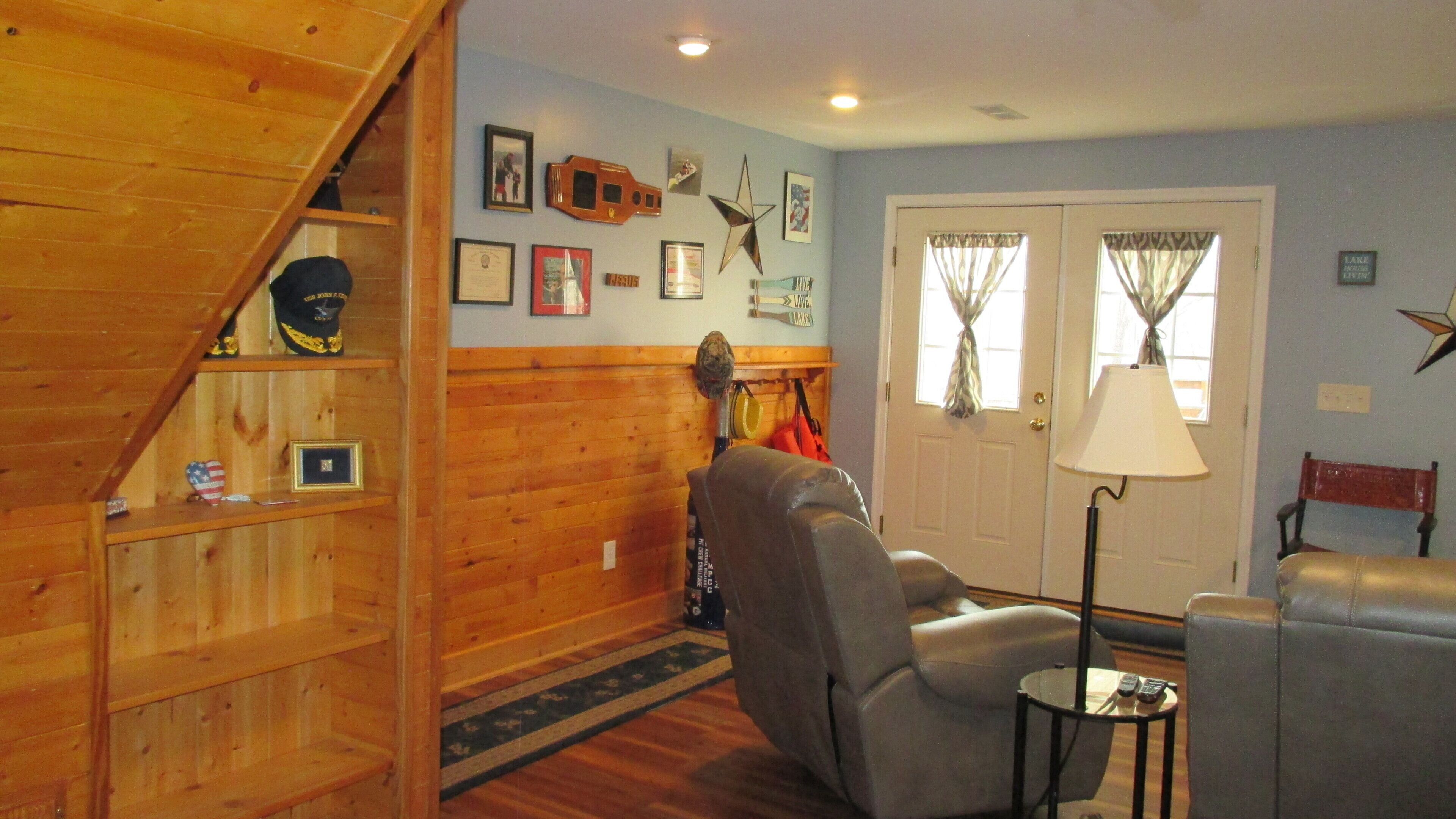 A living room with a wooden staircase, a gray armchair, a lamp, and a door with curtains.