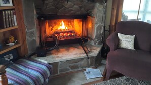 A stone fireplace with a fire, a television above it, and a cozy seating area with a cushion. - Beautiful waterfront lodge, private dock and breath taking views of Smith Mt. (Pittsville)