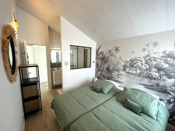 A bedroom with a large bed, a bathroom with a mirror, and a mural of a landscape.