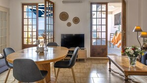 A living room with a round wooden table, two chairs, a flat-screen TV, and a sofa. - Casa Eden Roc (Brando)