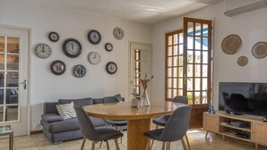 A living room with a round dining table, grey sofas, and a TV on a wooden cabinet. - Casa Eden Roc (Brando)