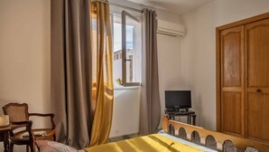 A bedroom with a bed, a television on a small table, a chair, and a wardrobe. - Casa Eden Roc (Brando)