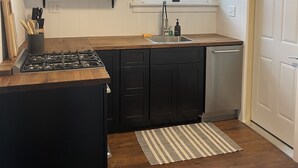A kitchen with wooden cabinets, a gas stove, a sink, and a window with a view of the outside.