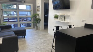 Una sala de estar moderna con un sofá, una mesa de comedor con sillas, un televisor montado en la pared y una planta en maceta.