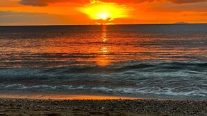 Un atardecer sobre un mar tranquilo con un litoral rocoso.