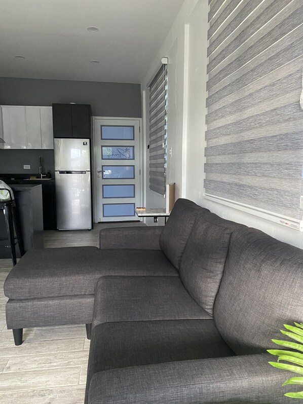 A modern living room with a grey sectional sofa, a small table, and a kitchen area in the background.