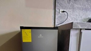 A compact refrigerator with a yellow tag, located in a corner of a room with patterned black and gray tiles. - Departameto Elegante y Cómodo (Cuenca)