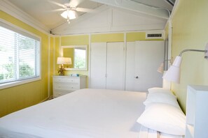 Quarto com cama, cômoda, espelho, ventilador de teto e janela com persianas.