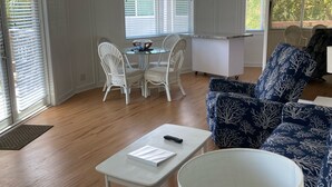 A modern living room with a glass dining table, white wicker chairs, a blue patterned sofa, and a white coffee table with a remote control. - Tropical Paradise (Islamorada)