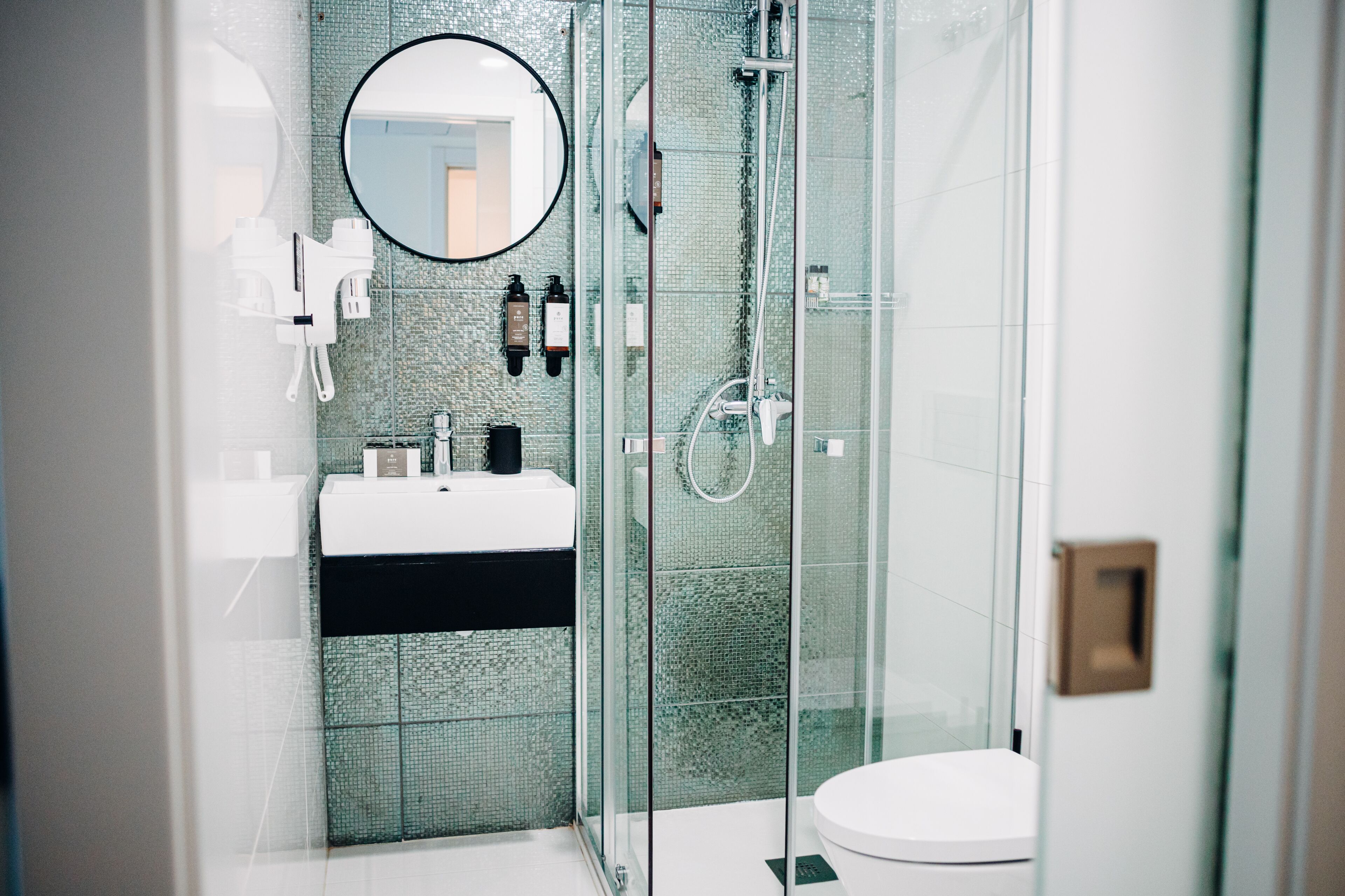 Une salle de bain moderne avec une douche à parois de verre, un lavabo blanc et un miroir rond.