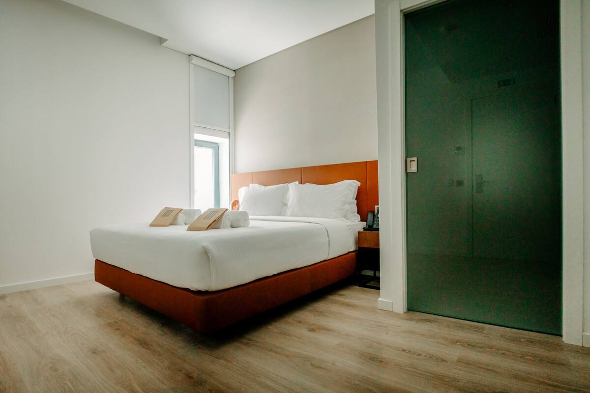 A modern hotel room with a large bed, wooden flooring, and a green door.