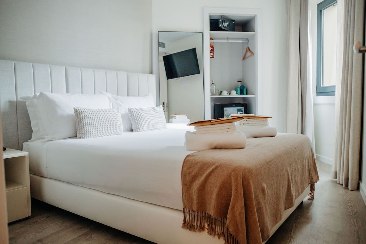 A neatly made bed with a white headboard, a brown throw blanket, and a stack of books on the bed.