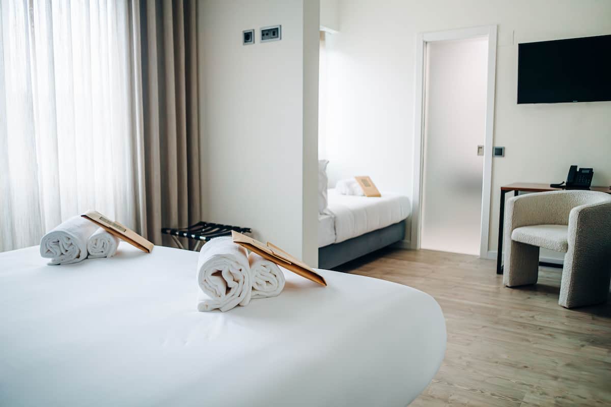 A hotel room with a large bed, a chair, a desk, and a TV on the wall.