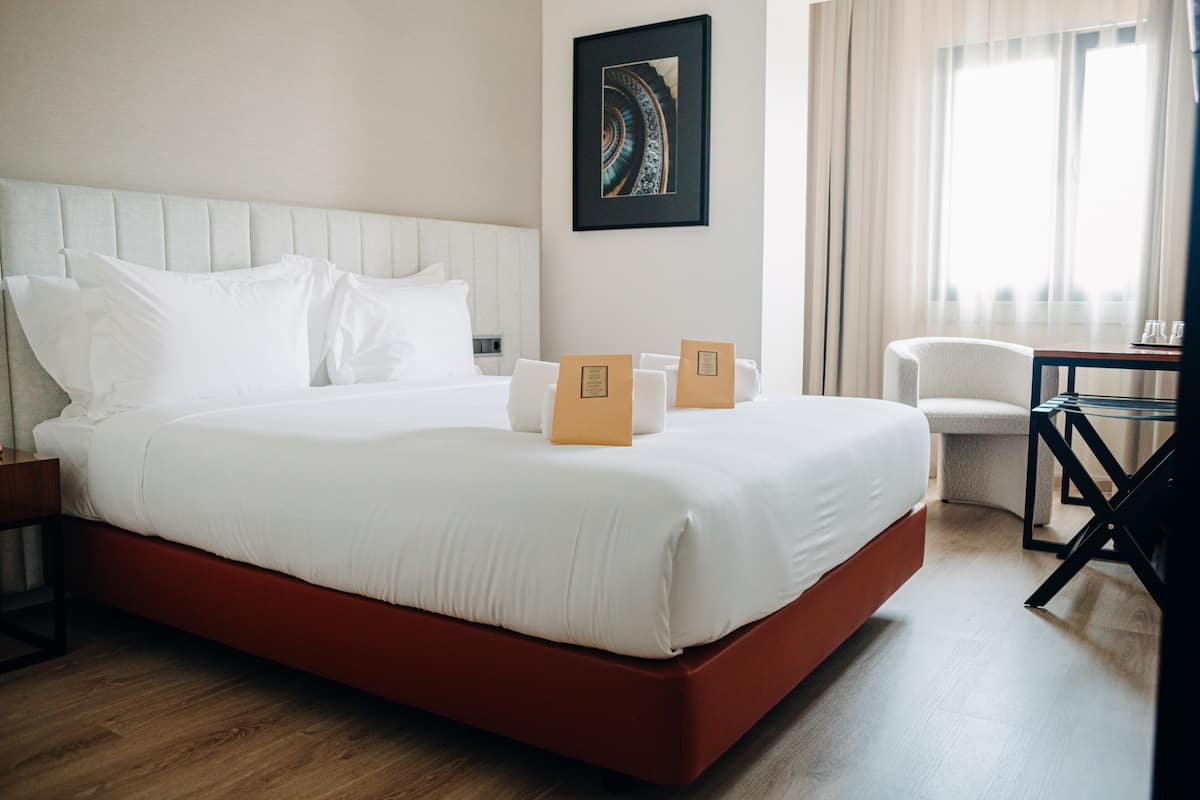 A neatly made bed with white linens, a red base, and two brown placards on the headboard.