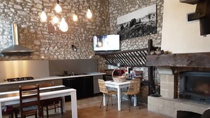 Una cocina moderna con pared de piedra, zona de comedor con sillas, mesa de vidrio y chimenea.