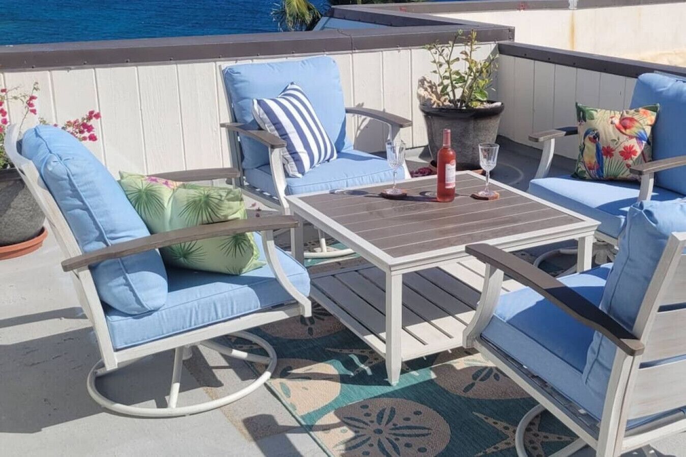 Une terrasse avec une table et des chaises, une plante en pot et une bouteille de vin rouge.
