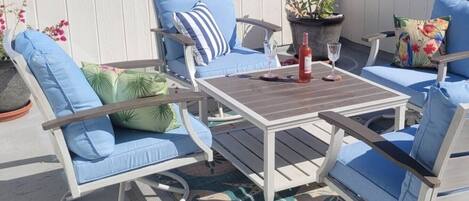 Une terrasse avec une table et des chaises, une plante en pot et une bouteille de vin rouge.