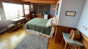 Ein gemütliches Schlafzimmer im Blockhausstil mit einem großen Bett, Holzbalkendecke, einem Schreibtisch mit Stuhl und einem kleinen Tisch.