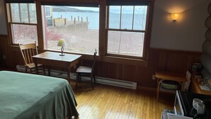 Ein gemütliches Cabin-Zimmer mit Bett, Tisch mit Lampe, Sitzbank und Seeblick.