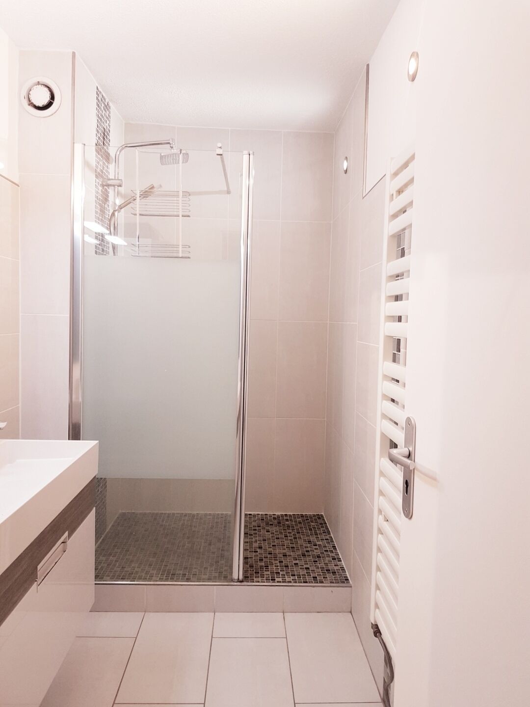 A modern bathroom with a glass-enclosed shower, a white sink, and a tiled floor.