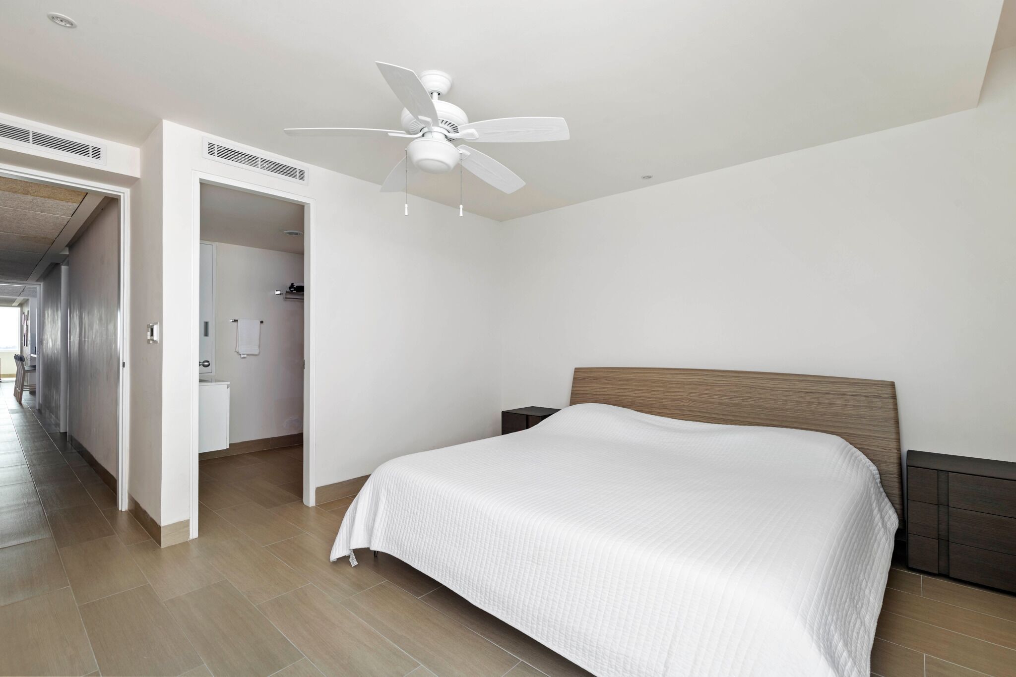 Una habitación de hotel moderna con una cama grande, un ventilador de techo y un cabecero de madera.