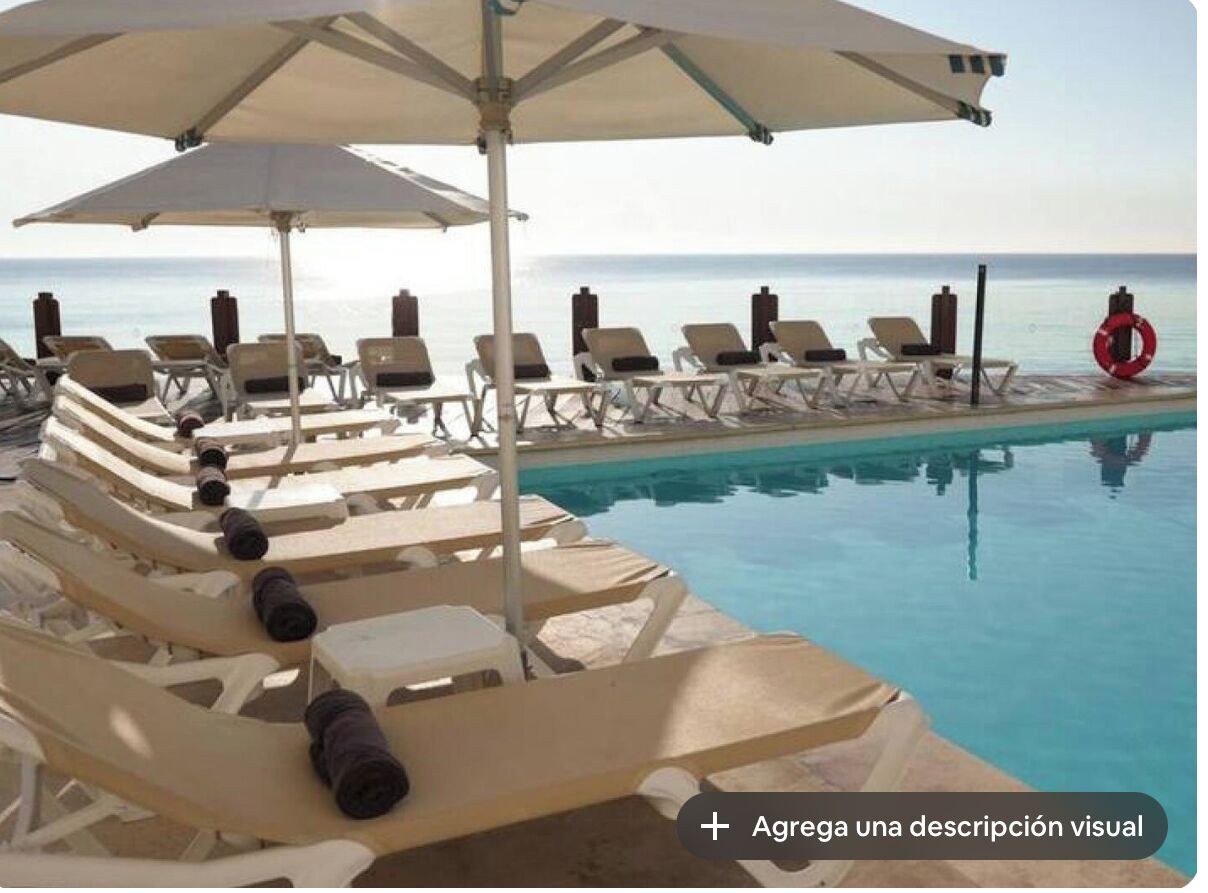 A poolside area with lounge chairs and umbrellas, a lifebuoy, and a clear view of the sea.