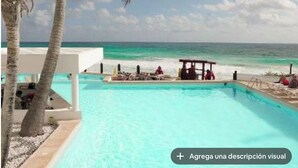 Un área de piscina con vista al océano, palmeras y una playa.