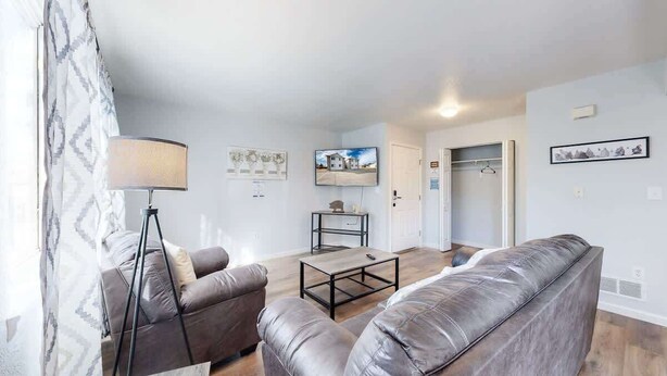 Un salon avec un canapé, une table basse et une lampe. Il y a une porte qui donne sur une autre pièce et un porte-manteau.