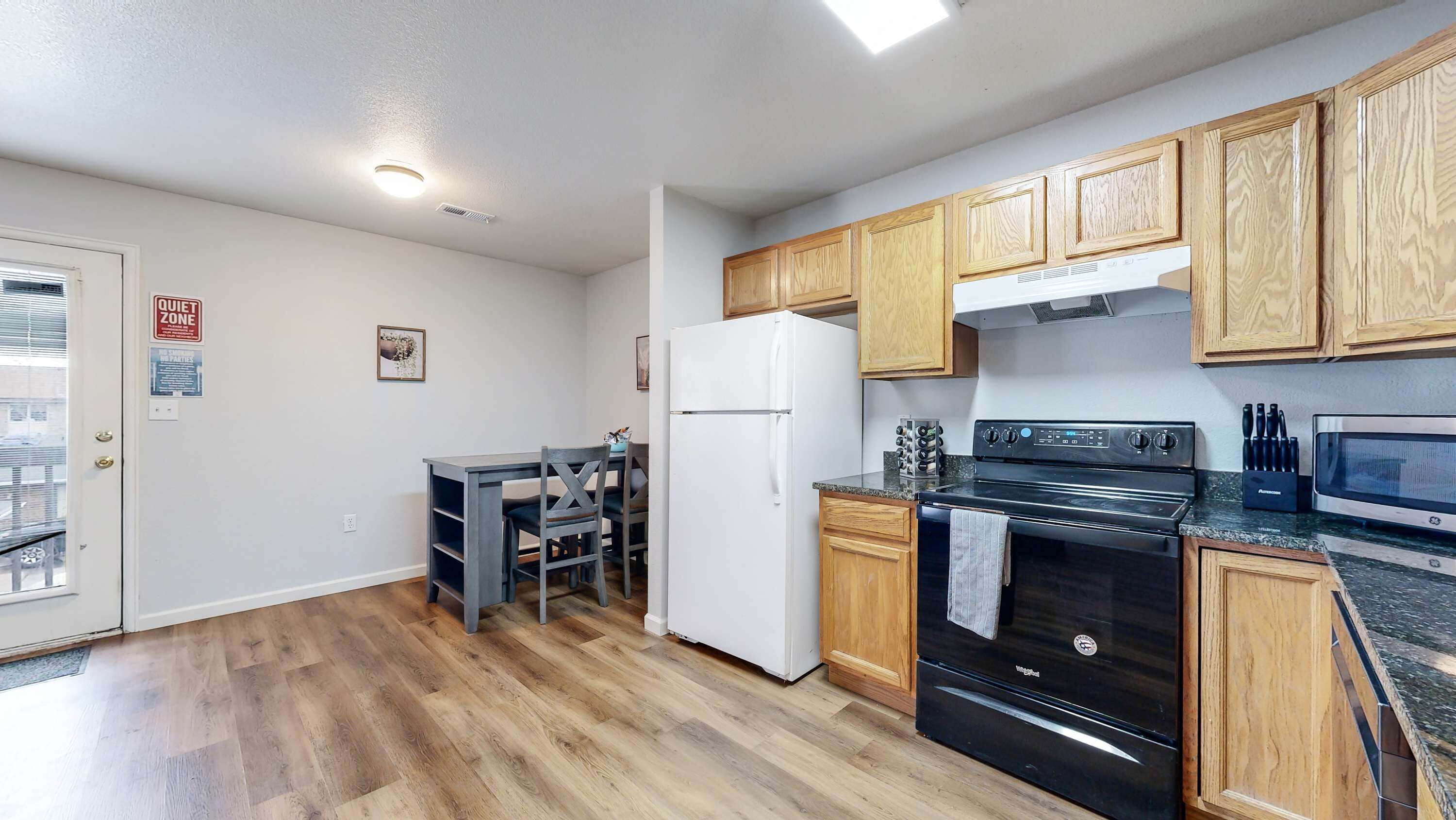 A kitchen with wooden cabinets, a refrigerator, stove, microwave, and a dining area with a table and chairs.