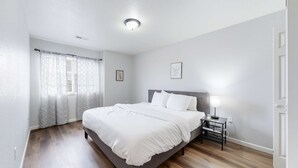 Une chambre à coucher avec un lit, une table de chevet avec une lampe, une fenêtre avec des rideaux et un luminaire au plafond.
