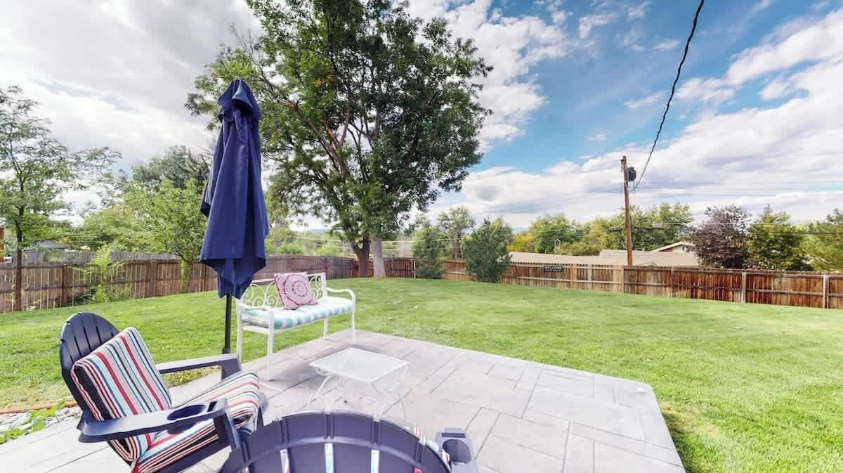 A backyard patio with a lawn, a chair, a table, and a blue umbrella.