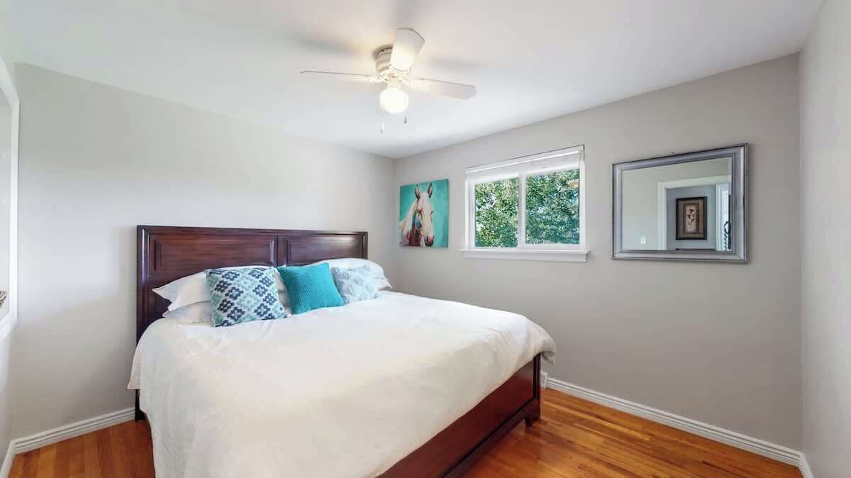 A bedroom with a bed, a ceiling fan, a window, and a framed mirror.