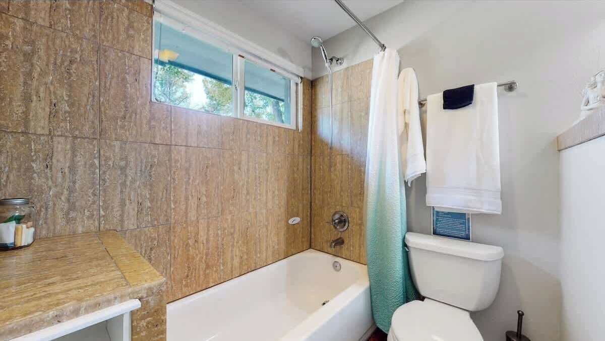 A bathroom with a bathtub, toilet, and a window.