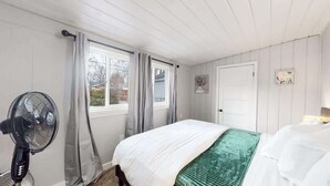 Un dormitorio con cama, ventilador, ventana con cortinas y puerta.