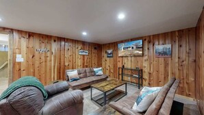 A cozy living room with wooden paneling, a brown leather sofa, a coffee table, and a television. - Spacious Arvada Home with King Beds and Office (Arvada)