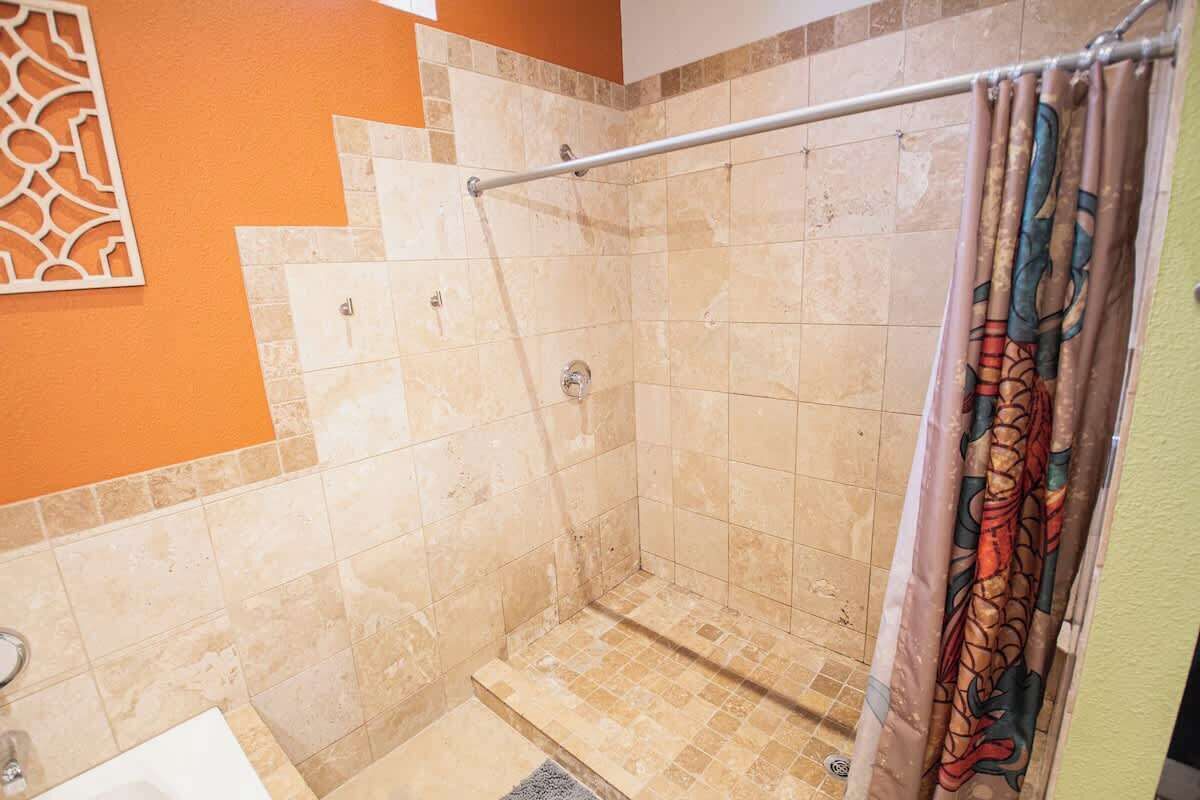 A shower with beige tiles, a metal grab bar, and a colorful shower curtain.