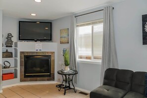 A living room with a fireplace, a television mounted above it, and a window with curtains. - Charming Family Home with Cozy Retreat (Denver)