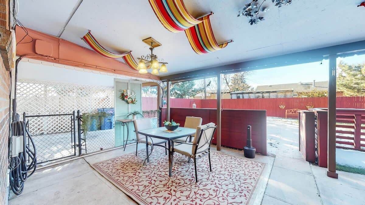 A covered patio area with a table and chairs, a patterned rug, and a ceiling with colorful drapes.
