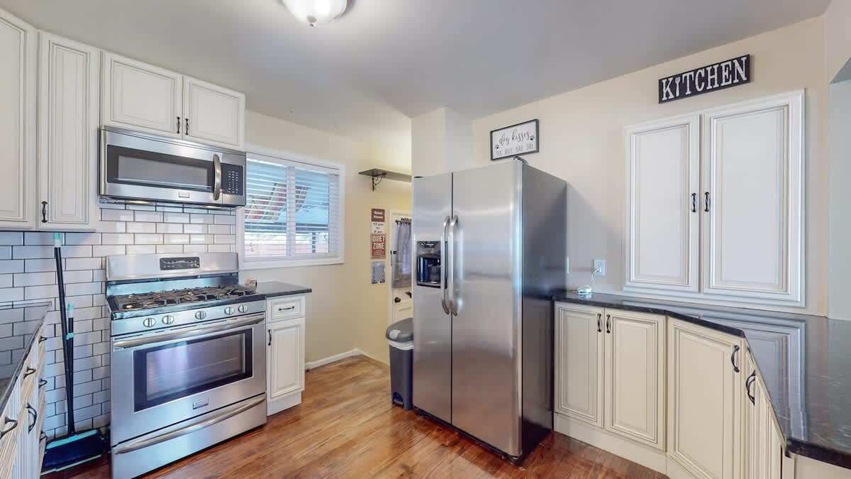 A kitchen with white cabinets, stainless steel appliances, and a wooden floor.