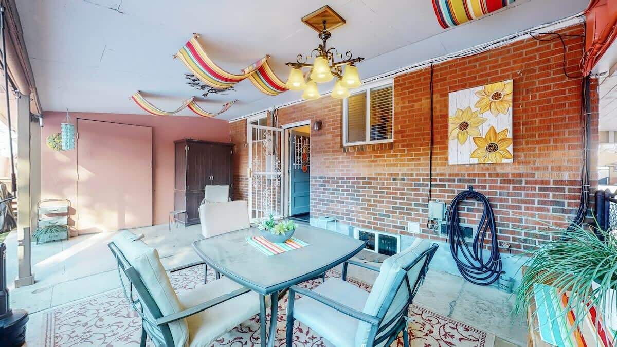 A dining area with a table and chairs, a hanging light fixture, and a brick wall with a flower painting.